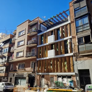 Imagen de la fachada completa desde un ángulo lateral, mostrando la integración de los paneles móviles y la vegetación, que redefine el paisaje urbano del barrio de Tetuán.