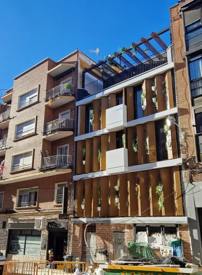 Imagen de la fachada completa desde un ángulo lateral, mostrando la integración de los paneles móviles y la vegetación, que redefine el paisaje urbano del barrio de Tetuán.