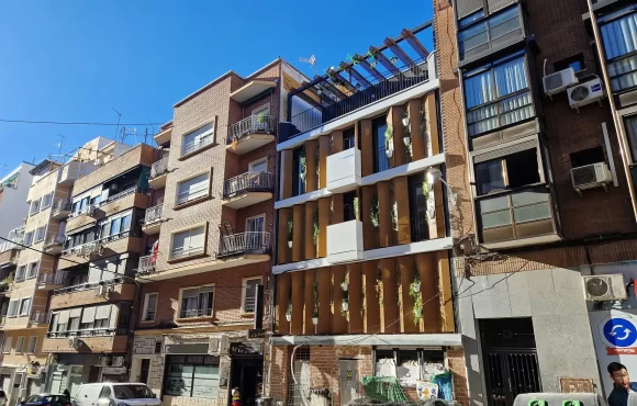 Imagen de la fachada completa desde un ángulo lateral, mostrando la integración de los paneles móviles y la vegetación, que redefine el paisaje urbano del barrio de Tetuán.