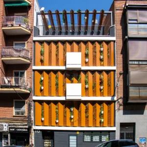Fachada de un moderno edificio residencial con paneles verticales naranjas y plantas colgantes en las paredes.