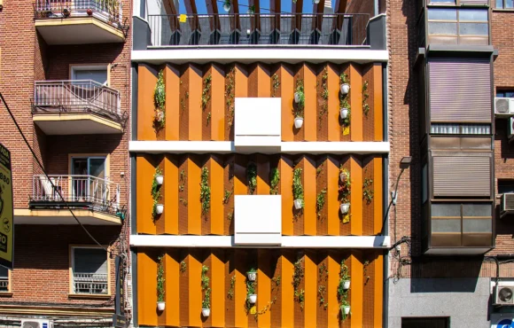 Fachada de un moderno edificio residencial con paneles verticales naranjas y plantas colgantes en las paredes.